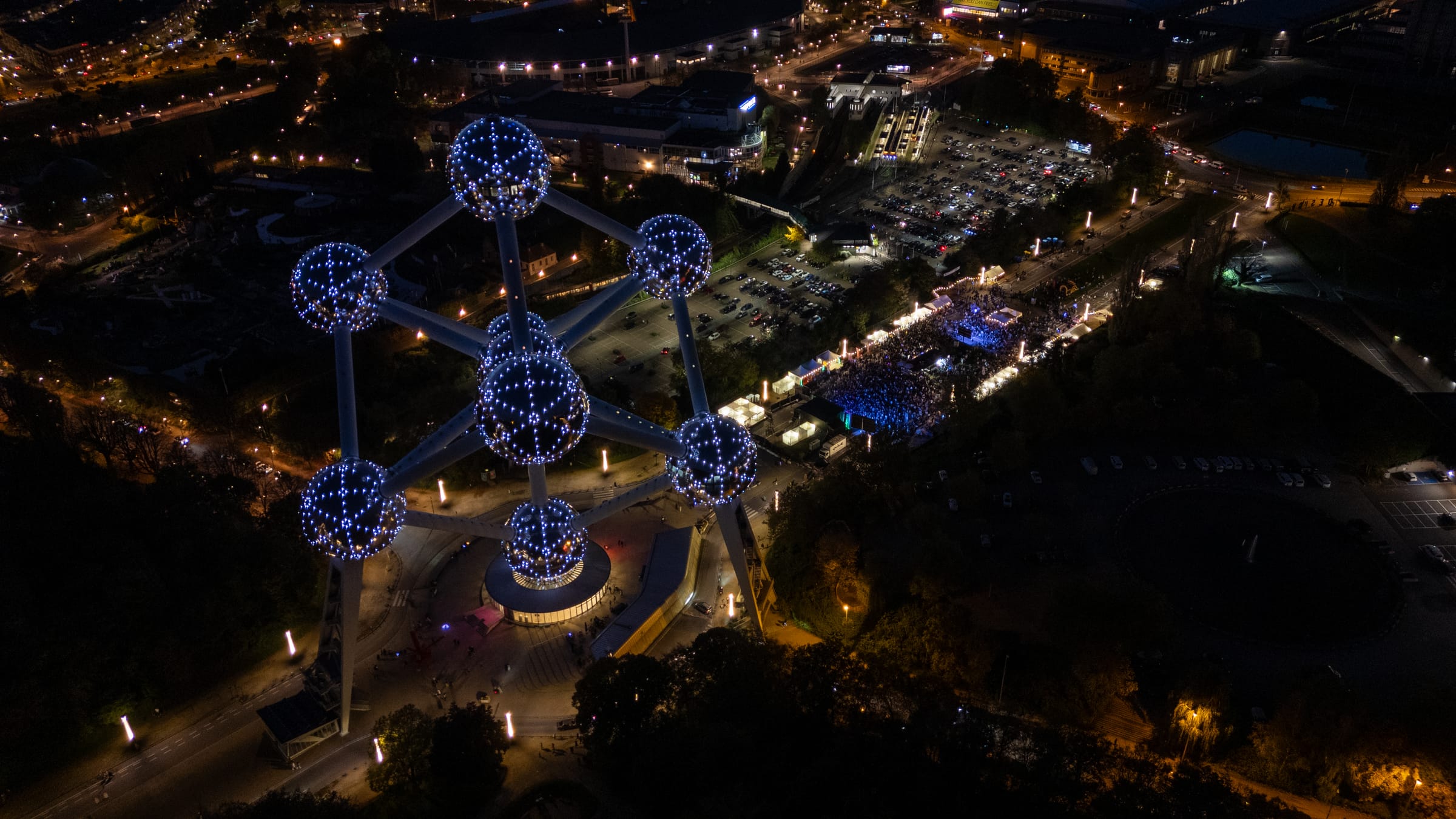 The Atomium lit at night, with the festival on the esplanade below